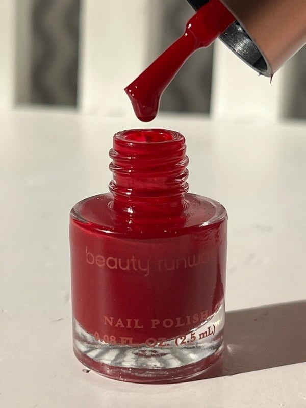 Red nail polish brush lifted above its bottle