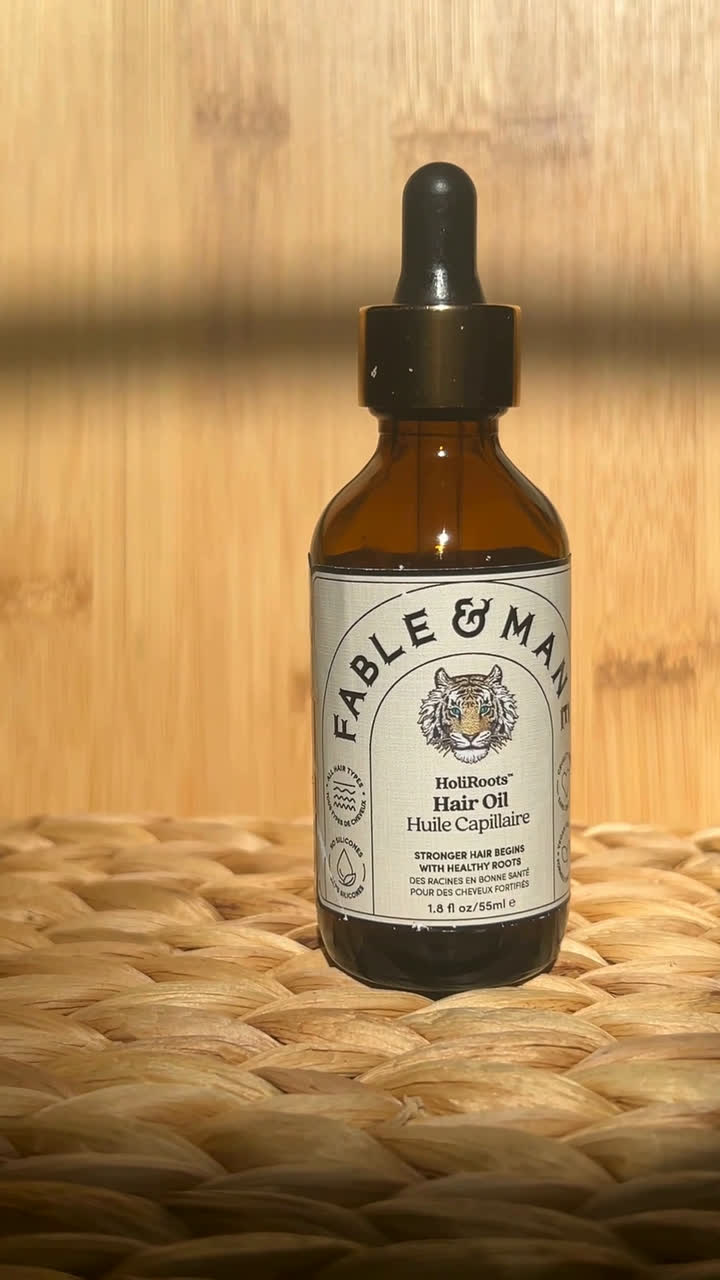 Fable & Mane HoliRoots hair oil bottle on a woven mat in warm light