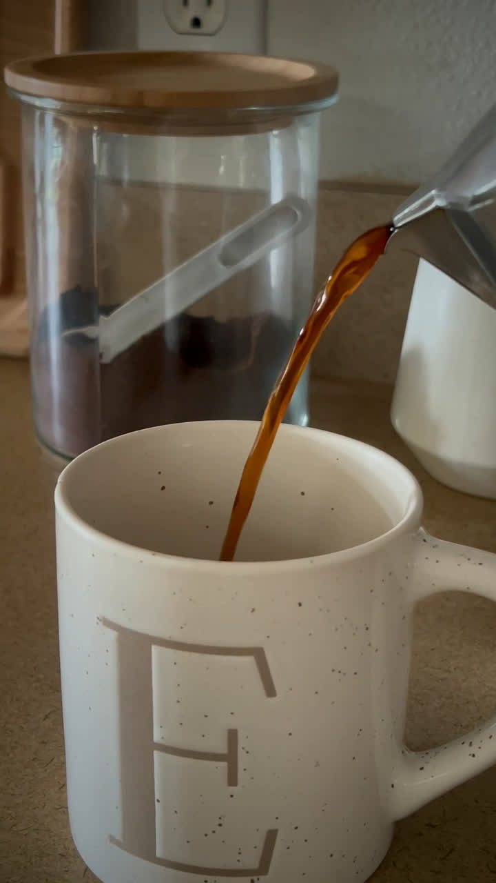 Coffee pouring from a moka pot into a monogrammed ceramic mug