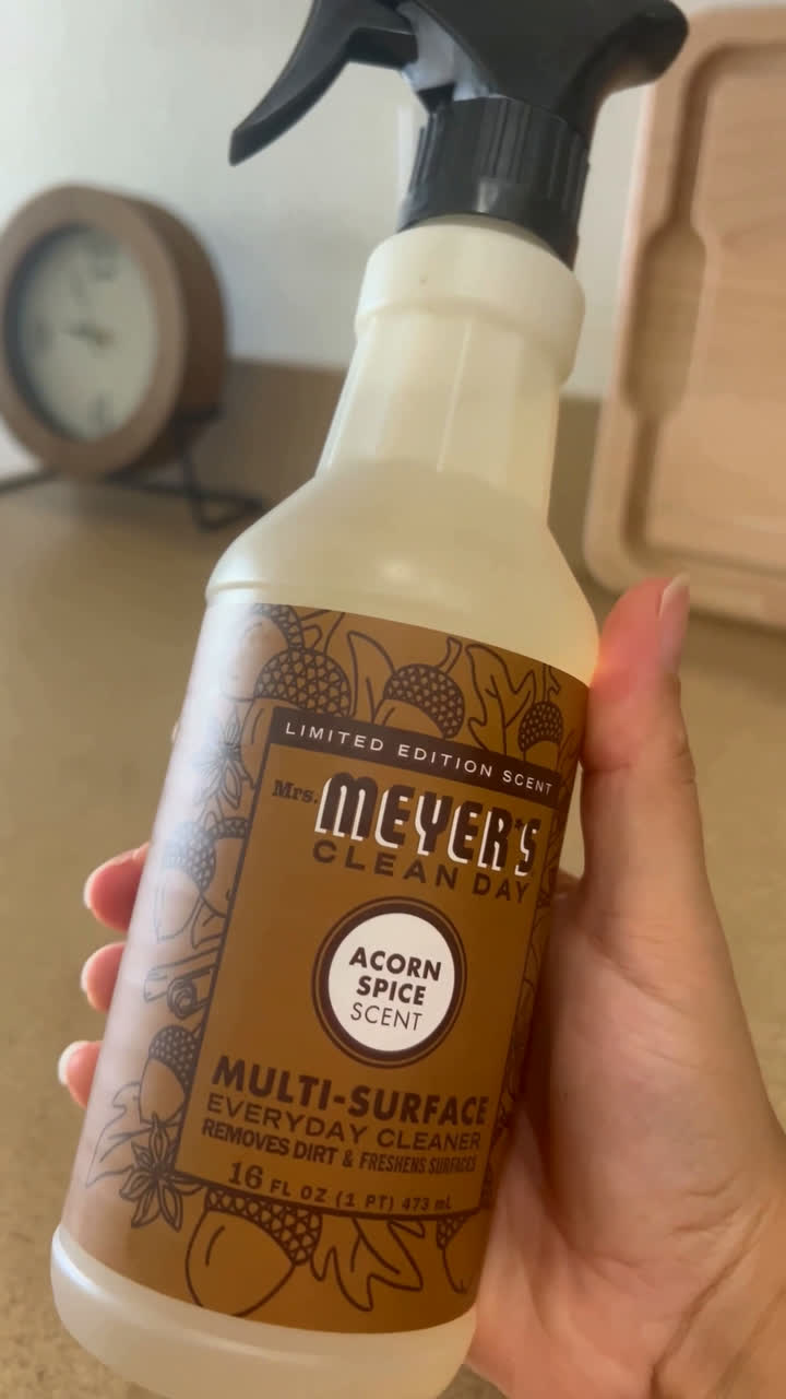 Hands holding a Mrs. Meyer's Clean Day Acorn Spice multi-surface cleaner spray bottle