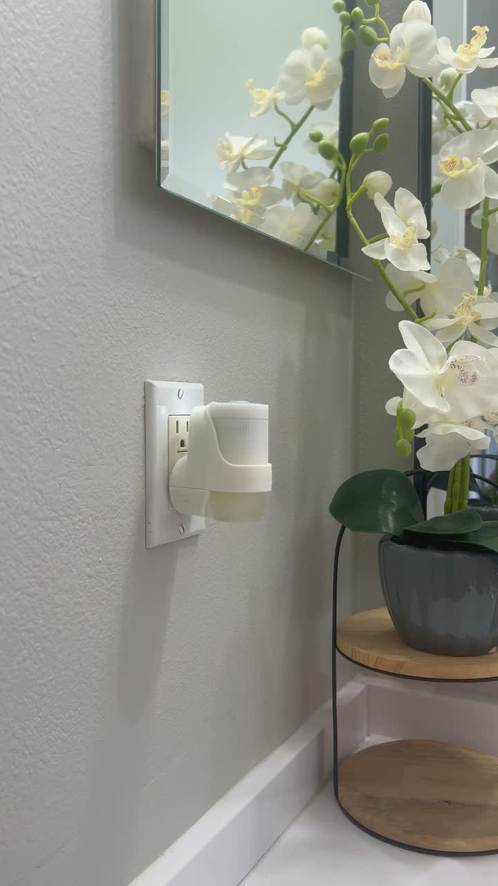 Mrs. Meyer's plug-in diffuser in a wall socket beside white orchids